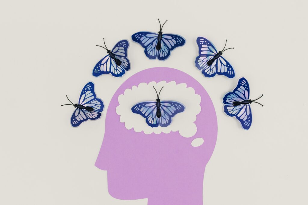 Ilustración de una cabeza en color lila con una mariposa azul en el cerebro y varias mariposas alrededor, simbolizando ideas o pensamientos en movimiento